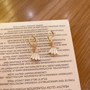 Detalle de pendientes de aro dorados con colgantes de volante de bádminton de esmalte