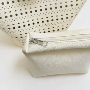 Close-up of a white hollow tote bag and its textured leather zipper pouch detail.