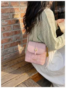 Stylish pink plaid crossbody bucket bag with heart clasp shown in a sunny outdoor setting