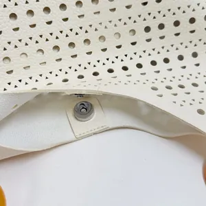 Detailed close-up showing the silver magnetic snap closure of a cream hollow-out tote bag.