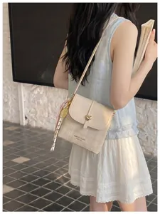 Elegant beige textured crossbody bag with gold heart buckle carried by a model