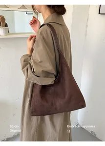 Braune Wildleder-Hobo-Tasche, getragen von einem Modell in einem hellen, minimalistischen Raum.