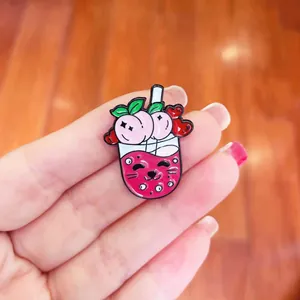 Detailed macro view of a cute cartoon peach milk tea enamel pin with cat face details
