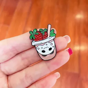 Close-up of a cute cat-faced strawberry bubble tea enamel pin brooch on a hand