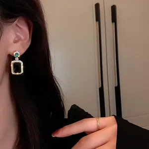 Detail of elegant emerald green square halo drop earrings on a model with golden finish