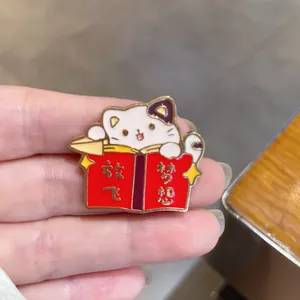 Detail of cute cartoon cat enamel pin badge reading a red book with gold engraving
