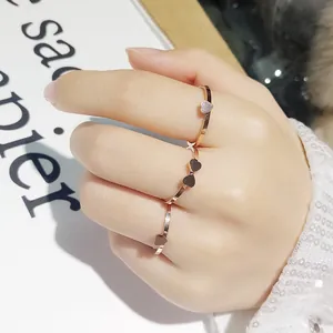 Détail de trois délicates bagues en or rose avec des motifs en forme de cœur sur une main.