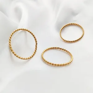 Close-up of three delicate gold-toned twisted rope stackable rings on white silk fabric.