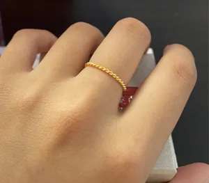 Detail view of a minimalist gold-plated stainless steel twisted rope ring worn on a finger.