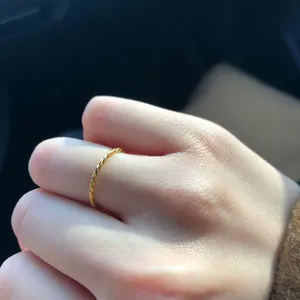 Close-up of minimalist gold twisted rope ring on finger, showing delicate metal texture