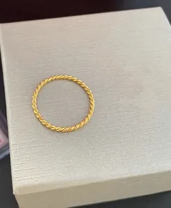 Close-up detail of a minimalist gold-plated twisted rope ring on a textured box