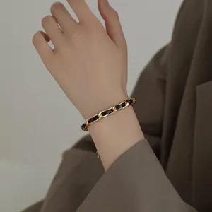 Detailed view of gold-toned titanium steel chain bracelet with black leather weave.
