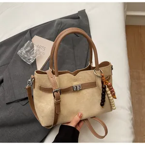 Elegant vintage beige suede handbag with leather accents and beaded charm on grey blazer.