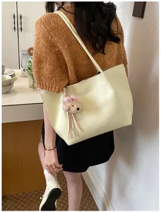 Close-up of a cream large capacity tote bag featuring a cute plush dog pendant detail.