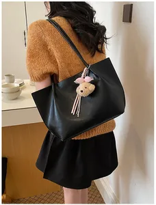 Back view of a model wearing a large black leather tote bag with a cute teddy bear pendant