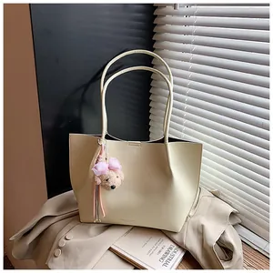 Large cream leather tote bag with pink bear charm presented on a beige blazer background