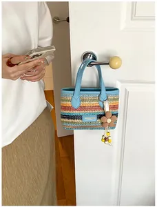 Bunte gestreifte gewebte Strohtasche hängt in einer Lifestyle-Szene an einem Türgriff