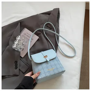 Close-up of a light blue tweed bucket bag featuring a gold heart buckle and thin shoulder strap