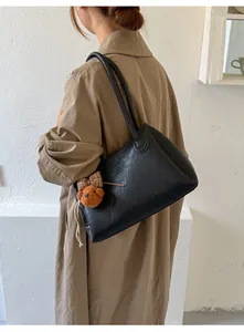 Side view of a vintage black leather tote bag with a brown bear charm accessory