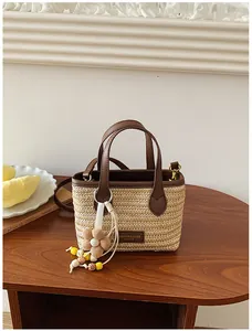 Stilvolle handgefertigte Stroh-Eimertasche mit braunen Ledergriffen und Blumenanhänger