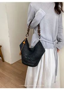 Detail view of a black hollow-out tote bag with wooden bead handles and orange tassel