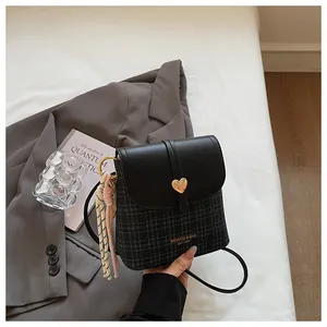 Detail of black plaid bucket bag with golden heart buckle and colorful woven charm