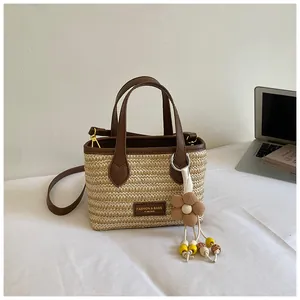 Detailansicht einer Stroh-Eimertasche mit braunem Ledergriff und Blumenanhänger.