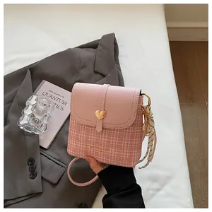 Close-up of pink tweed bucket bag with gold heart detail and striped scarf accessory