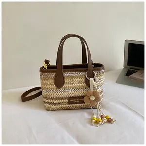 Detailansicht einer gewebten Stroh-Eimertasche mit Blumenanhänger und braunen Ledergriffen