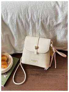 Close-up of stylish off-white checkered bucket bag with gold heart clasp and tennis charm