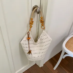 Detail view of a white hollow-out tote bag with wooden bead handle hanging on a door.