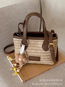 Exklusive handgewebte Stroh-Eimertasche mit braunem Lederbesatz und Blumenanhänger