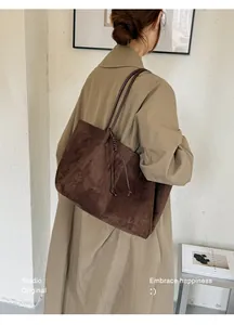 Back view of a large brown suede tote bag worn on the shoulder with a beige coat