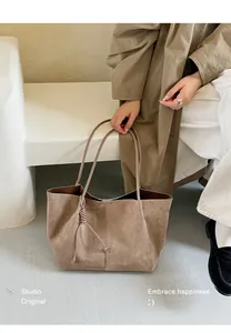 Large brown suede tote bag held by a model showcasing its soft texture and spacious design.