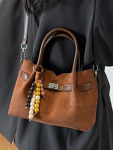 Stylish brown suede tote bag with wooden bead charm worn over a black blazer.