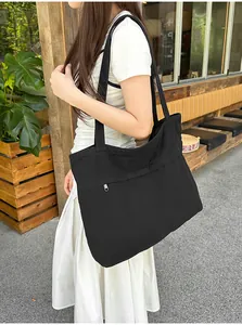 Grande borsa tote in tela nera con design a pieghe e zip frontale indossata da una modella.