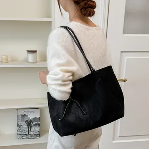 Large black suede tote bag with drawstring detail carried by a model in indoor setting