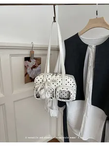Detail view of a vintage-style white polka dot shoulder bag featuring a pearl bow charm