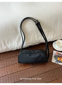 Black minimalist nylon shoulder bag presented on wooden floor in cozy interior scene