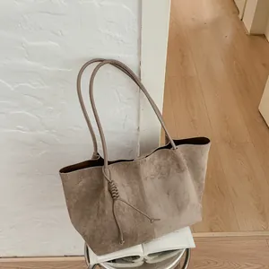 Detail view of a large khaki suede tote bag with elegant knotted tassel in a chic home setting