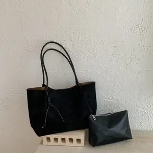 Close-up of black suede-style tote bag and matching pouch set on minimalist stone pedestal