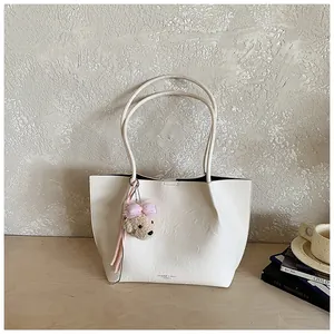 Detail view of off-white leather tote bag with cute teddy bear charm on wooden desk.