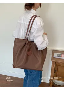 Vue détaillée d'un sac cabas en nylon marron avec breloque cœur porté à l'épaule.
