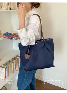 Mannequin portant un grand sac cabas en nylon bleu marine à côté d'une étagère à livres.