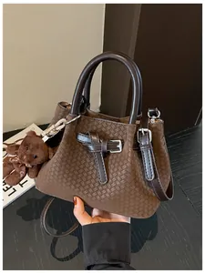 Detailansicht einer braunen Eimertasche mit Webmuster und einem Teddybären-Anhänger.