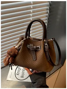 Detailansicht einer braunen Retro-Handtasche mit Flechtstruktur und Plüschbärchen.