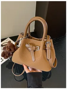 Nahaufnahme der eleganten braunen Eimertasche mit Webmuster und süßem Bärenanhänger Zubehör