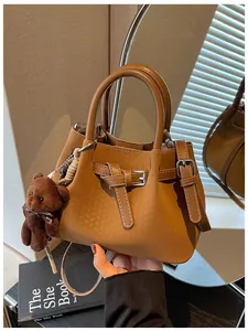 Detailaufnahme der braunen Handtasche mit Webmuster, Vintage-Schnalle und Bärenanhänger