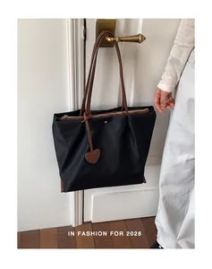 Sac cabas en nylon noir avec anses marron et breloque cœur sur une poignée de porte.