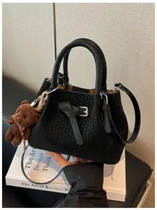 Modische schwarze Handtasche mit Flechtstruktur und einem süßen Bärenanhänger auf Buch